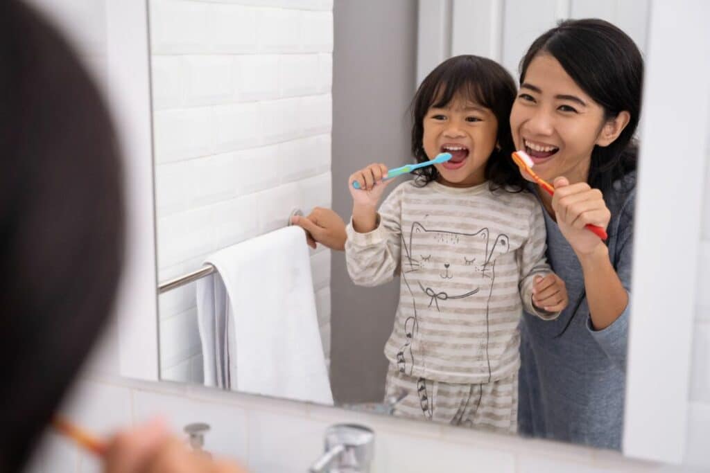 Kid brushing her teeth with her mum